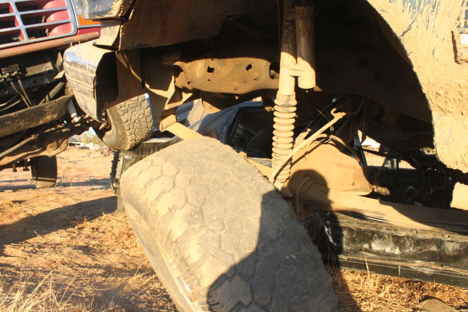 Undercarriage view of a muddy truck with a tire in the foreground. Another vehicle is partially visible on the left