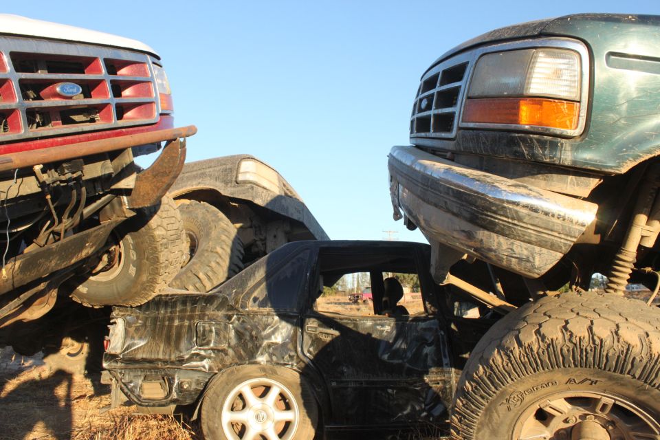 Two trucks are stacked on top of a wrecked car, with large tires visible