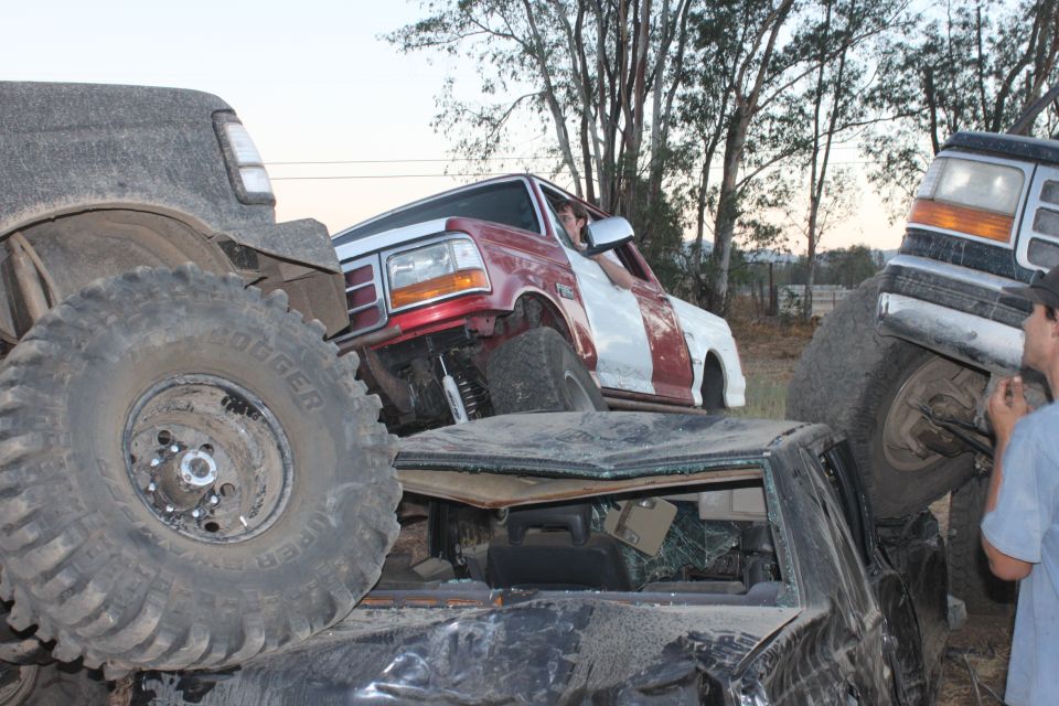 Red and white truck stuck on top of other vehicles, with a gray truck on the left and another truck on the right