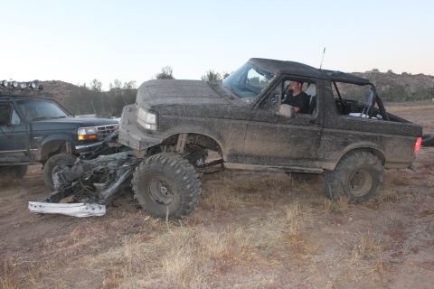 Mud-covered 1992 Ford Bronco with front-end damage next to another SUV