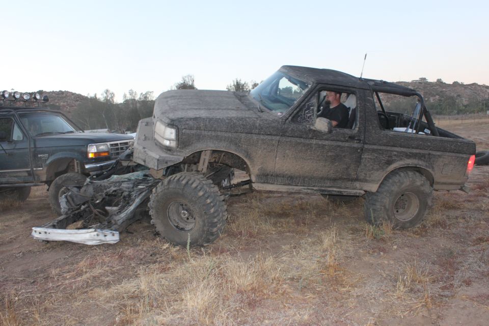 Mud-covered 1992 Ford Bronco with front-end damage next to another SUV