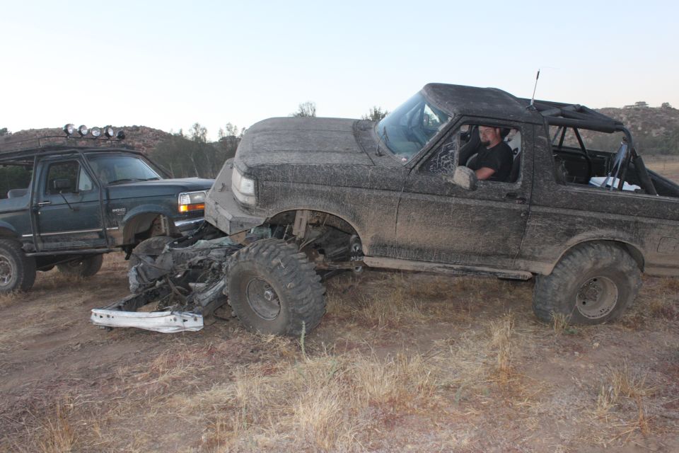 Damaged black 1992 Ford Bronco with a crushed front end, next to a green Ford truck