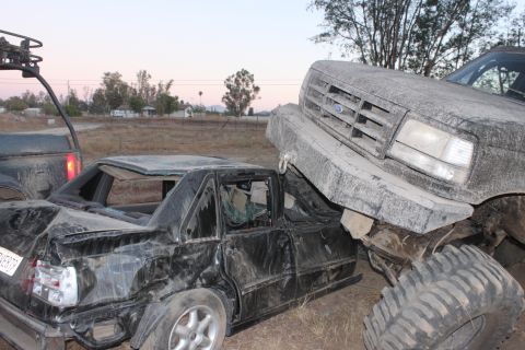 Large Ford truck on top of a crushed black sedan. The truck's grille is visible