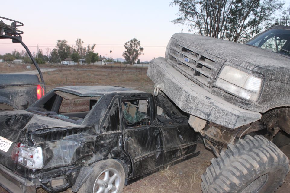 Large Ford truck on top of a crushed black sedan. The truck's grille is visible