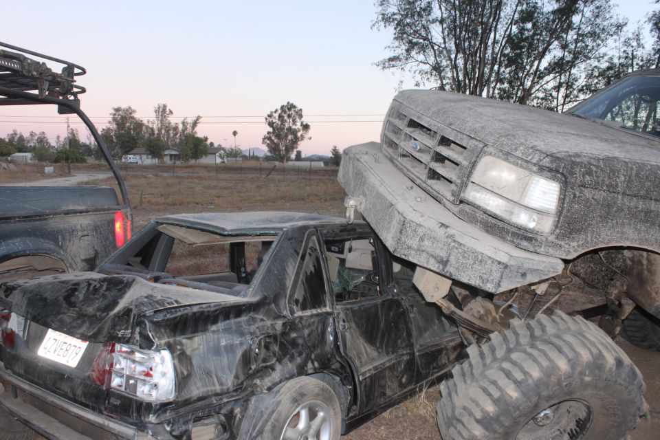 Big truck on top of a crushed car. Another truck is to the left