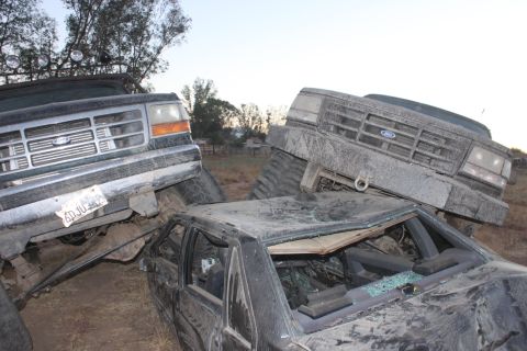 Two 1992 Ford Broncos, one dark green and one grey, are piled on top of a crushed black car