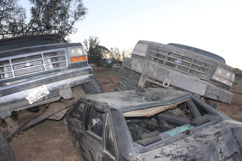 Two 1992 Ford Broncos, one dark green and one grey, are piled on top of a crushed black car