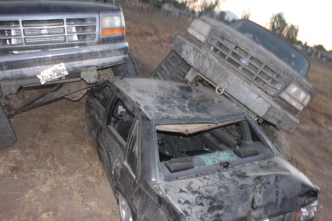 Two Ford trucks on top of a wrecked car. 1992 Ford Bronco