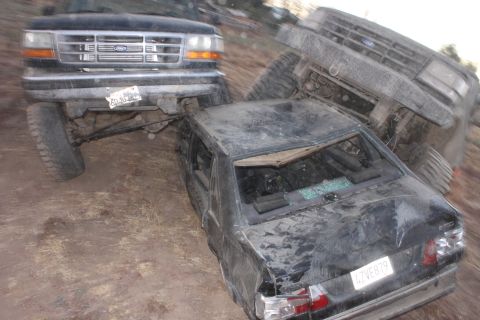 Ford F-Series truck on top of a black sedan, another truck is in the background