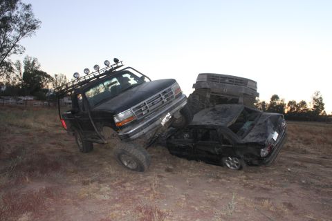 Black 1992 Ford Bronco on top of a wrecked black sedan, with a third vehicle behind
