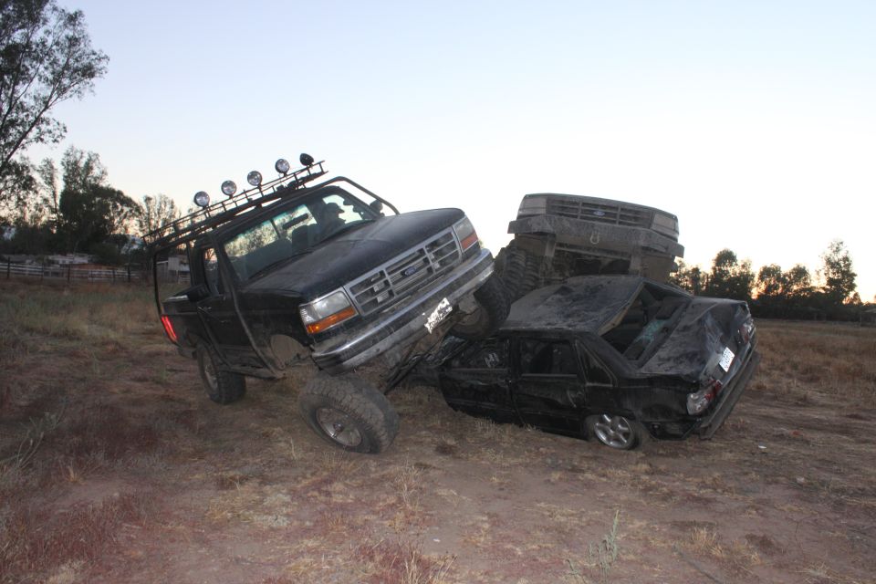 Black 1992 Ford Bronco on top of a wrecked black sedan, with a third vehicle behind