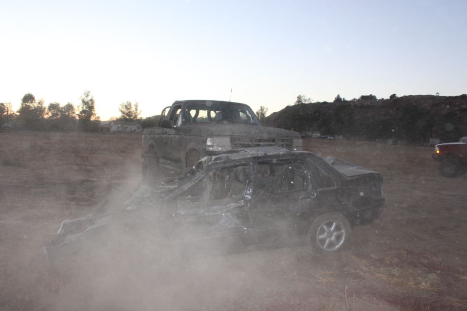 1992 Ford Bronco behind a crushed car in a dusty outdoor scene