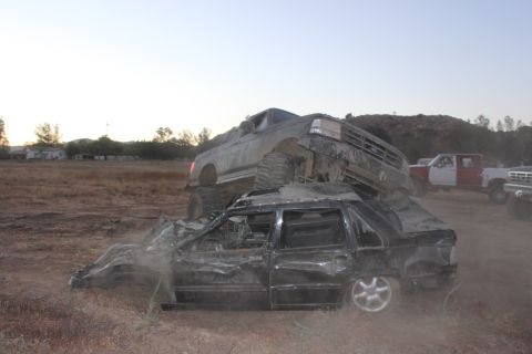 1992 Ford Bronco on top of a crushed sedan, with other trucks in background