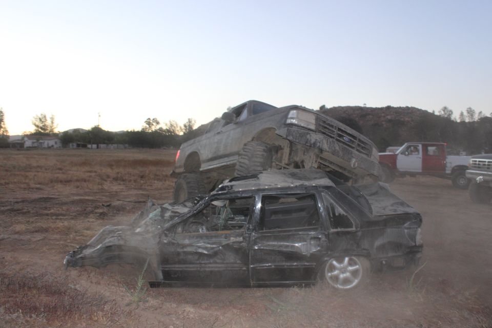 1992 Ford Bronco on top of a crushed sedan, with other trucks in background