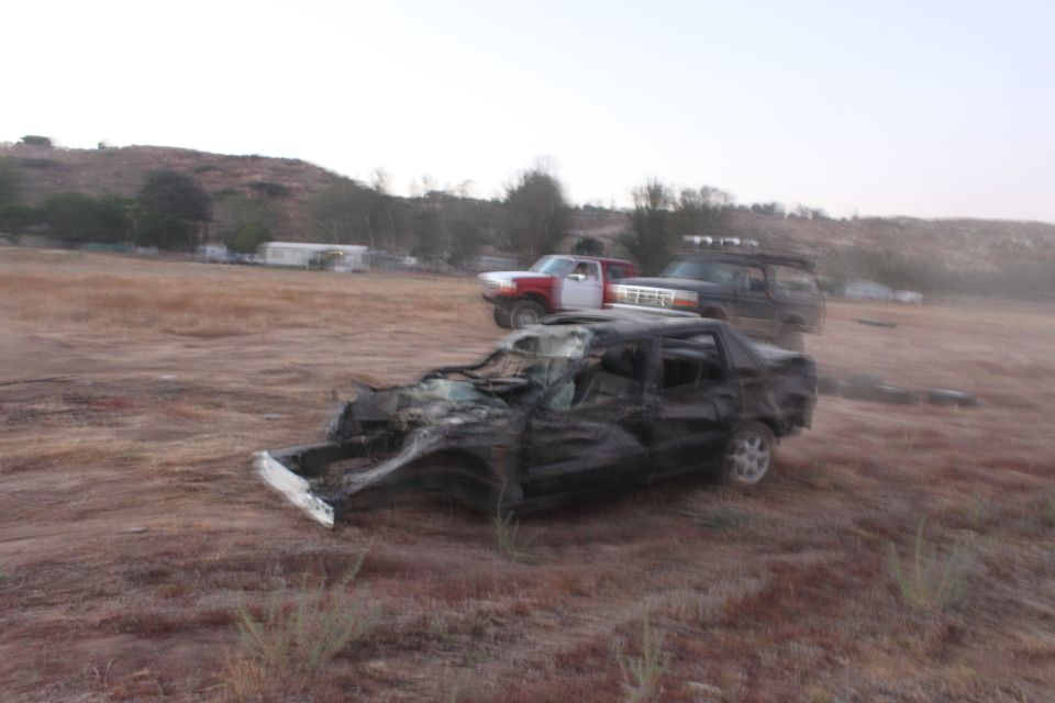 wrecked black car in foreground, red and white truck and dark SUV behind it in a dry field