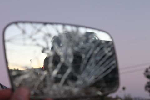 Reflection of a dark SUV in a cracked side mirror at dusk