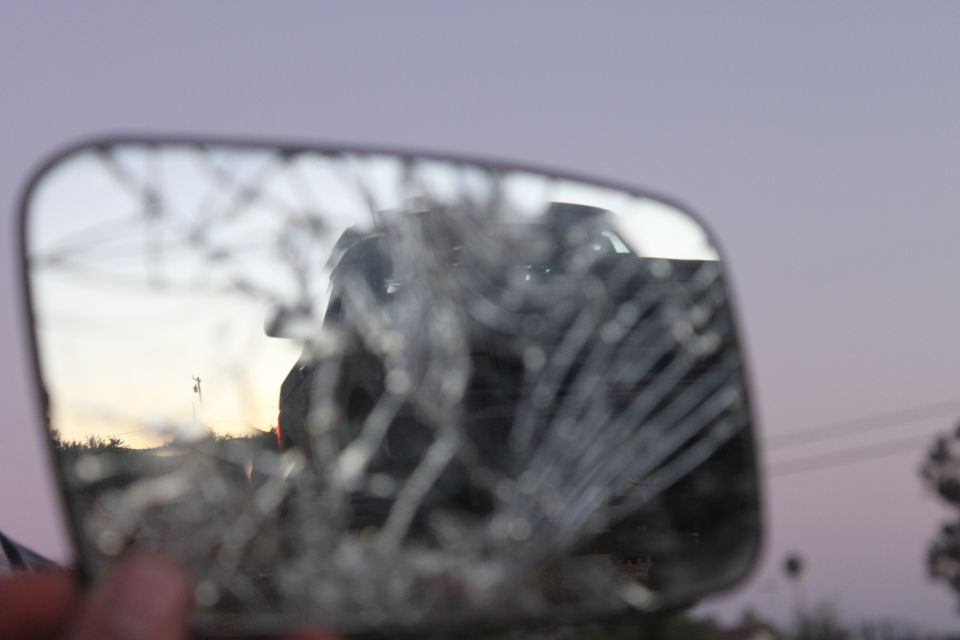 Reflection of a dark SUV in a cracked side mirror at dusk