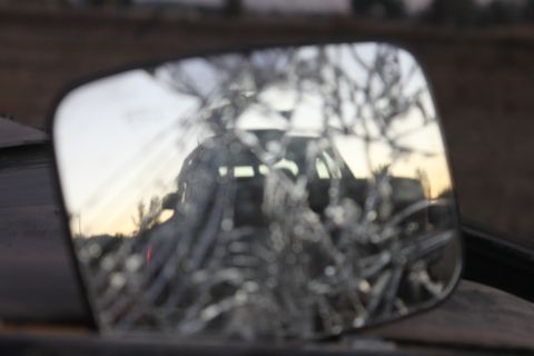 Cracked side mirror reflecting a dark SUV with a horizontal light bar