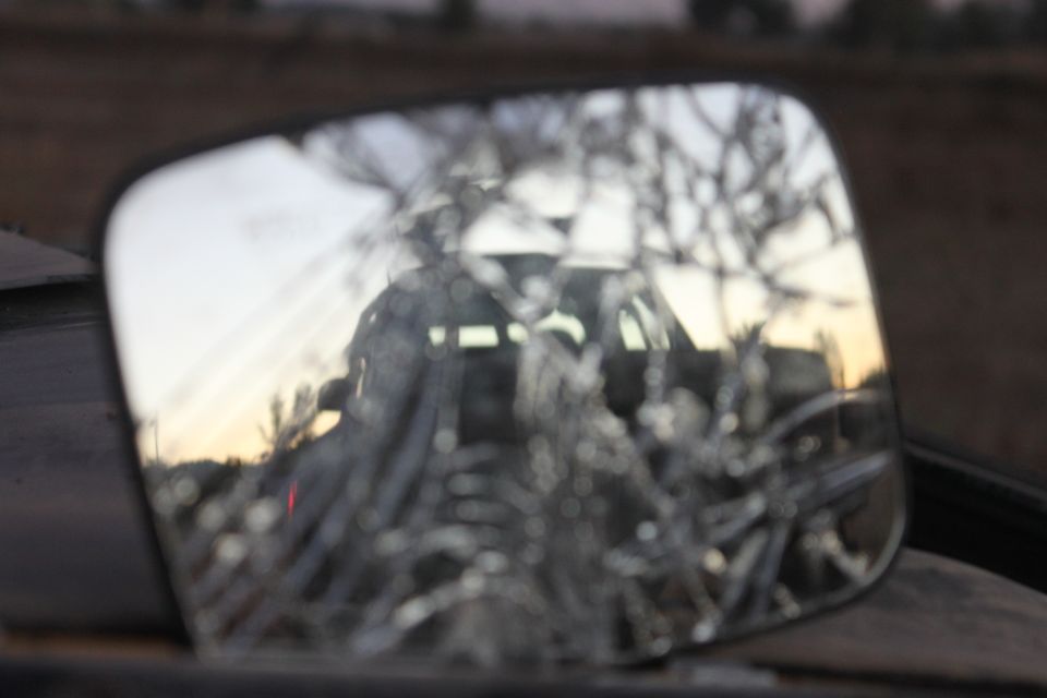 Cracked side mirror reflecting a dark SUV with a horizontal light bar