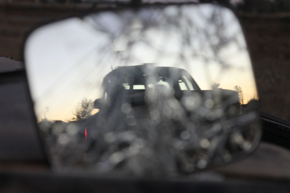 Dark SUV reflected in side mirror at sunset