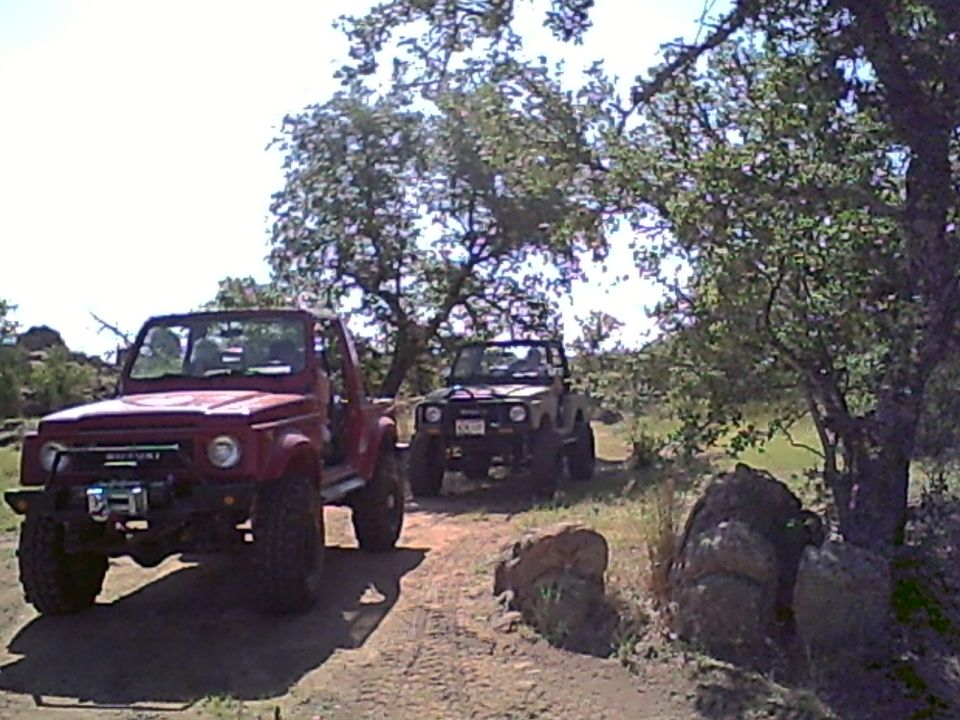 Red lifted topless Suzuki Samurai with winch bumper on a dirt trail with another 4x4 ahead
