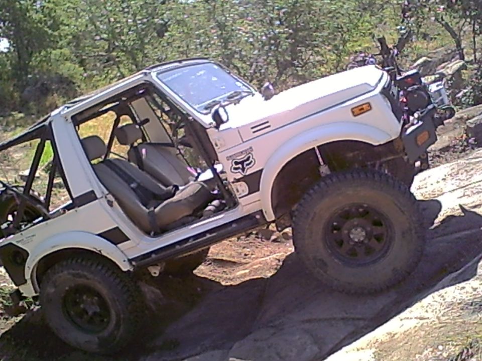 White lifted Suzuki Samurai with doors off climbing rocks on a trail