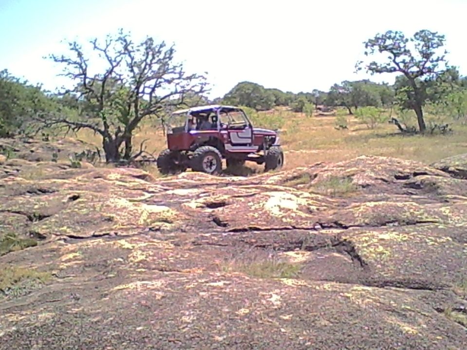 Red off-road vehicle with a roll cage parked on a rocky landscape with sparse trees