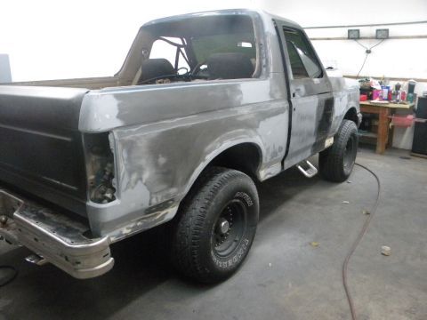 1987 Ford Bronco - This Ford pickup truck is undergoing body repairs, with primer applied to various panels and the rear taillight assembly removed.