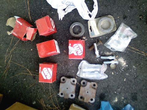 1990 Ford Bronco - A collection of automotive parts, including several red boxes with white logos and various bolts and washers, laid out on a dark, paved sur…