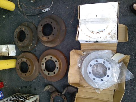 1990 Ford Bronco - Several brake rotors, some new and some used, are laid out on the ground.