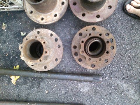 1990 Ford Bronco - Close-up of old, rusty vehicle wheel hubs and a drive shaft resting on asphalt.