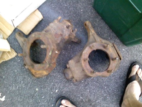 1990 Ford Bronco - Two heavily rusted automotive parts are shown on a dark asphalt surface.