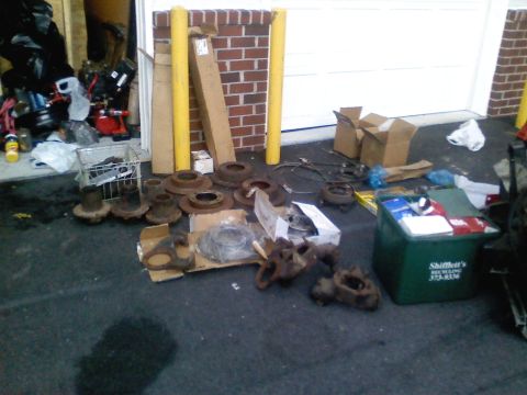 1990 Ford Bronco - Assorted vehicle parts, including brake rotors and hubs, are laid out on the ground near a garage.