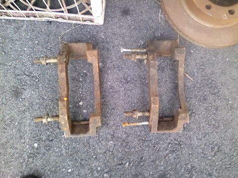 1990 Ford Bronco - Pair of used brake caliper brackets and a brake rotor on the ground.
