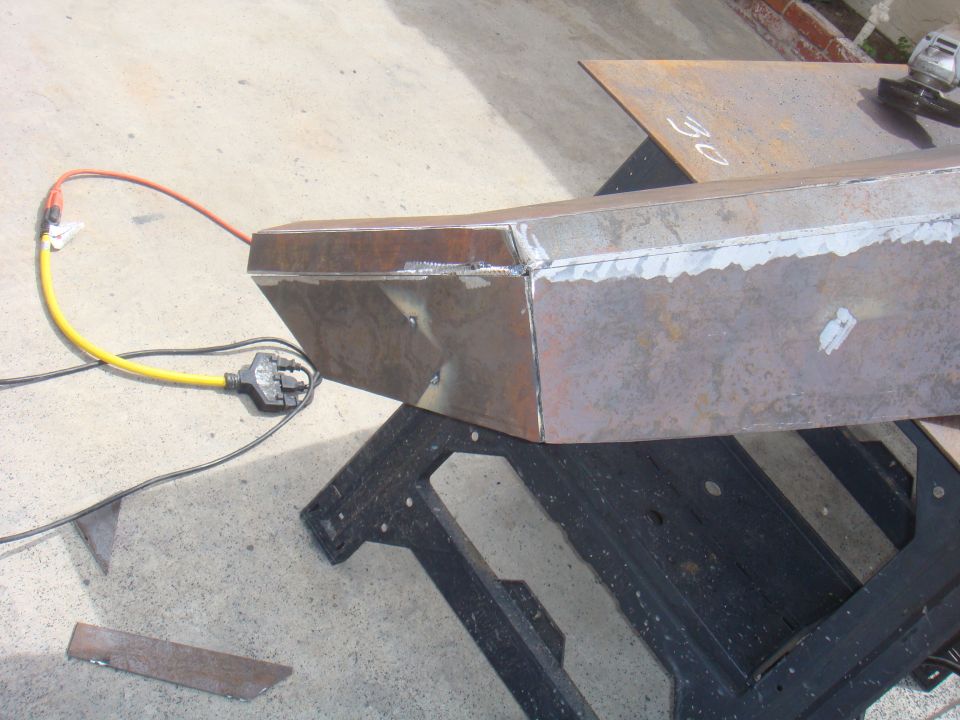 Welded steel bumper section on sawhorses, with power cord and grinder nearby