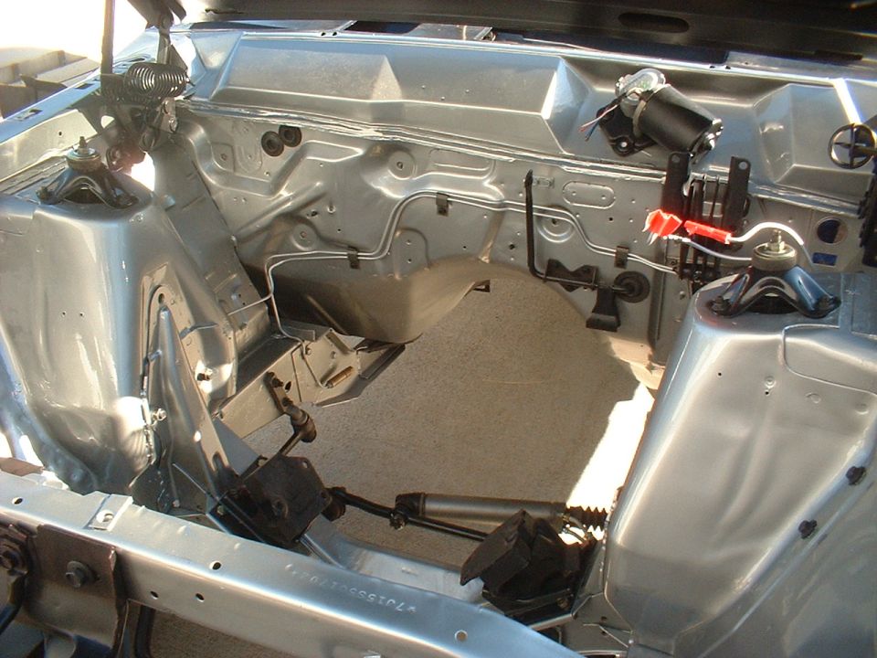 Empty silver-gray engine bay of a classic car with exposed shock towers and firewall