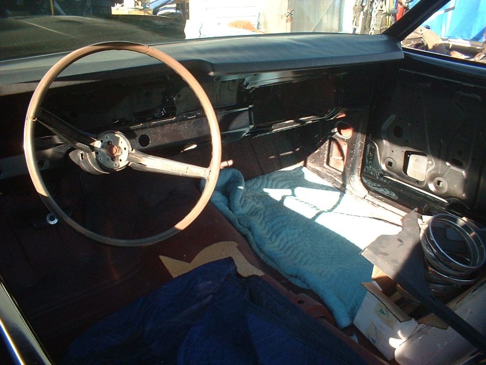 Gutted car interior with two-spoke steering wheel and bare rusty dash and floor