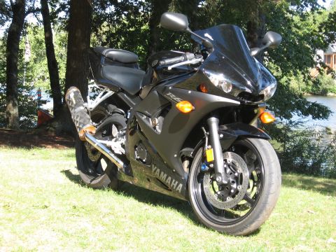 2008 Yamaha R1 - A black Yamaha R6 motorcycle is parked on a grassy area next to a body of water, with trees in the background.