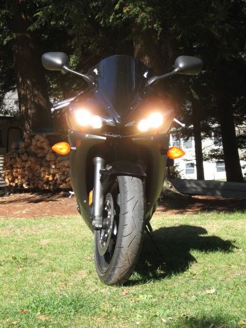 2008 Yamaha R1 - Motorcycle front view with headlights on, parked on grass with trees in background.