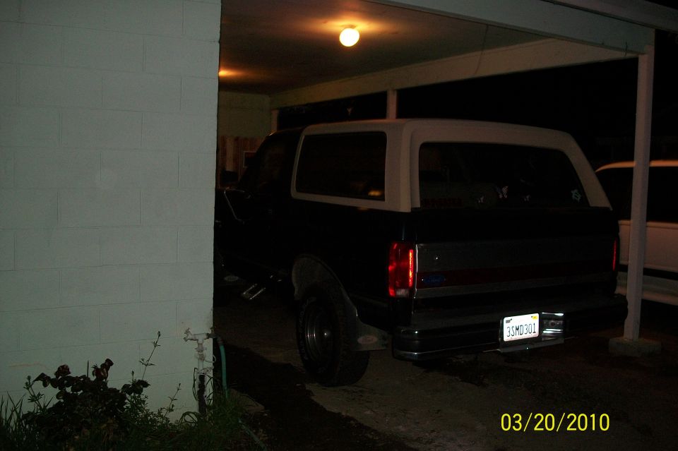 Dark Ford Bronco with tan top parked in carport at night, rear three-quarter view, CA plate 3SMD301