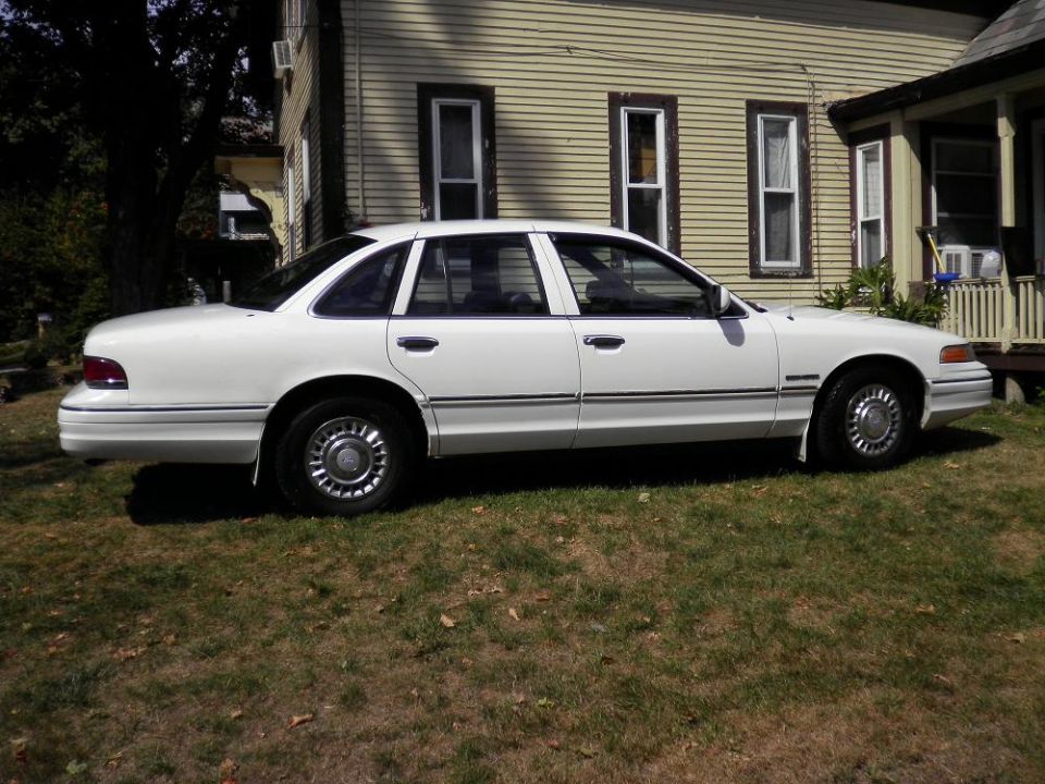 White sedan parked on grass in front of a house. Visible chrome hubcaps and body trim
