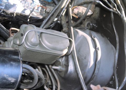1976 Ford Ranchero - Tight engine-bay shot of a cast-iron dual-bowl brake master cylinder with its stamped-steel bail-wire retainer clamping the lid, mounted to…
