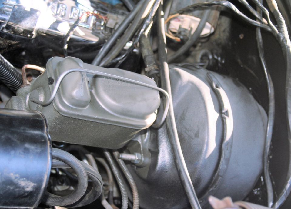 Dual-bowl brake master cylinder with bail-wire lid clamp on black vacuum booster