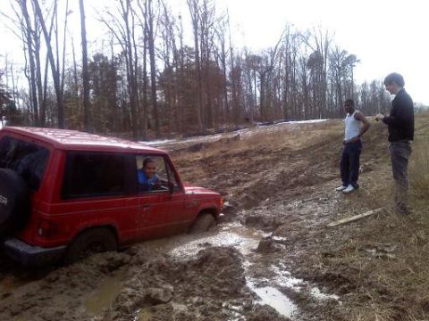 1992 Ford Bronco - A red SUV is stuck in a muddy off-road trail with two people observing the situation.