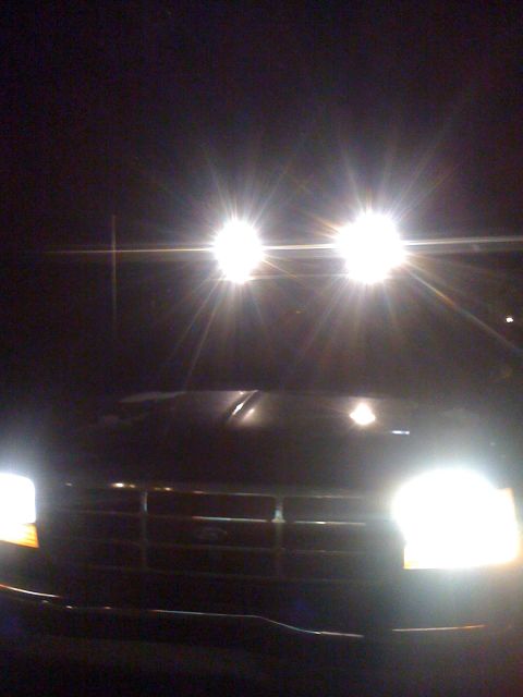 1992 Ford Bronco - The front grille of a 1992 Ford Bronco is visible at night, illuminated by its bright headlights.