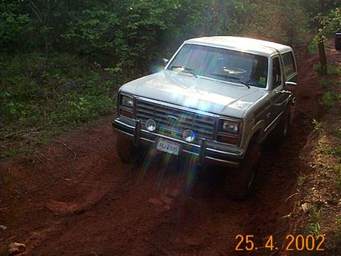 1986 Ford Bronco - A 1980s Ford Bronco navigates a muddy, wooded path.