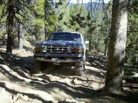 1996 Ford Bronco - A 1996 Ford Bronco navigates a challenging, rocky trail through a forest.