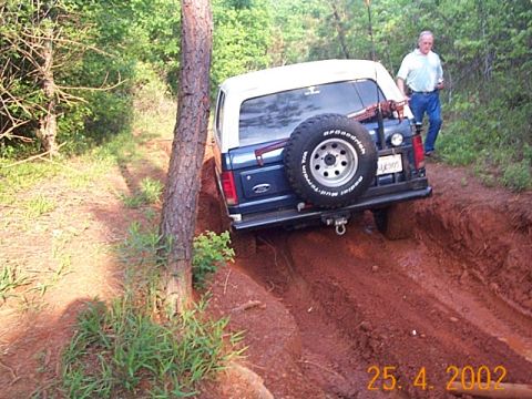 1986 Ford Bronco - An SUV navigates a challenging muddy trail with a man standing nearby.