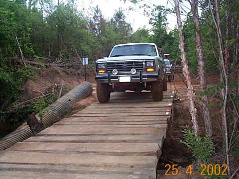 1986 Ford Bronco - Ford F-Series truck navigates a rough wooden bridge crossing in a wooded area.