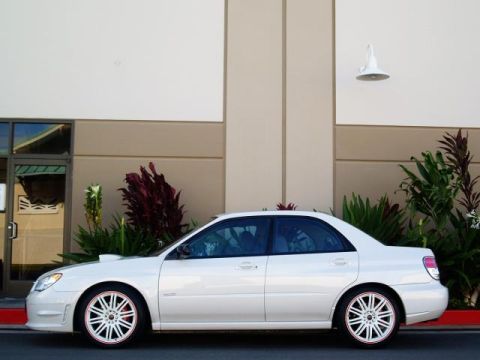 2007 Subaru Impreza - A white sedan is parked outside a building with lush green plants in the background.